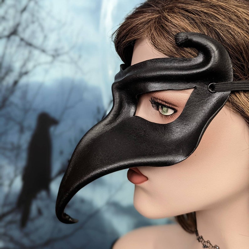 May include: A black leather masquerade mask with a long, curved nose. The mask covers the eyes and part of the forehead.