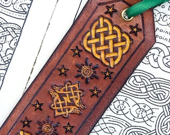 Könnte beinhalten: Ein braunes Leder Lesezeichen mit einem keltischen Knotendesign, Sternen und Sonnensymbolen. Das Lesezeichen hat ein grünes Band.