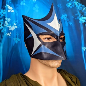 May include: A blue and white leather mask with a pointed top and a star design. The mask covers the eyes and nose, and has a small opening for the mouth.