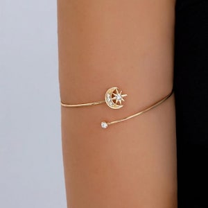Peut inclure: Un bracelet de bras doré au design ouvert, orné d'un motif de croissant de lune et d'étoile incrusté de cristaux transparents. Une extrémité de la fine tige métallique se termine par un petit cristal rond, tandis que l'autre porte le motif.