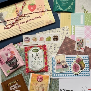 Może przedstawiać: Zestaw upominkowy z artykułami papierniczymi i herbatą, zawierający przewodnik Cozy Crea Club, herbatę Pukka Breathe In, herbatę English Tea Shop Rooibos Cocoa & Vanilla, herbatę Teekanne Caramel Apple Pie, herbatę Natural Temptation, taśmę washi, naklejki i papier.