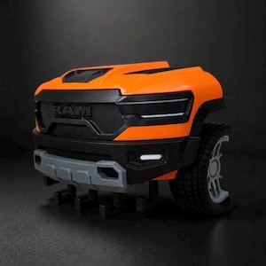 Puede incluir: Una parte delantera de camión de juguete en color naranja brillante y negro con el logotipo RAM en relieve en la parrilla. El componente del vehículo incluye un parachoques delantero gris, neumáticos negros texturizados y luces blancas.