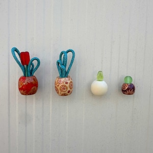 May include: Four decorative items are displayed against a white background. Two small, round vases with blue rope handles hold wooden tulips. Two small, round perfume bottles with glass stoppers are also shown.