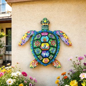 May include: A colorful, decorative turtle wall hanging. The turtle features a vibrant design with a green shell, blue and yellow accents, and floral patterns. The artwork is mounted on a beige wall, surrounded by flowers.