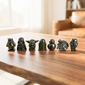 Op de afbeelding: Een set van zeven kleine, glanzend zwarte beeldjes die verschillende Star Wars-personages en voertuigen uitbeelden, waaronder Darth Vader, Yoda, R2-D2, BB-8, een Stormtrooper en de Millennium Falcon, opgesteld op een houten oppervlak.