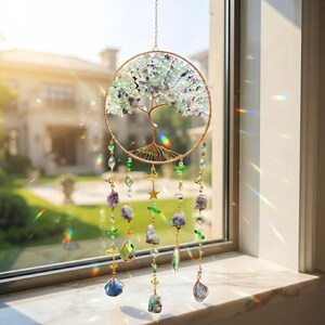 May include: A circular suncatcher featuring a wire-wrapped tree of life design with green and purple stone chips for leaves. Hanging from the bottom are multiple strands of gold-toned wire, small green beads, a gold star, and various crystal pendants.