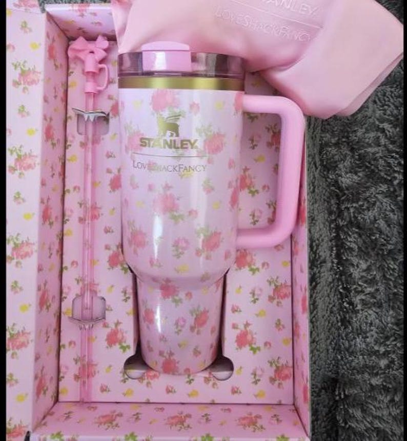 May include: A pink Stanley tumbler with a floral pattern, a pink handle, and a matching straw. The tumbler is in a floral-patterned box with the text "Stanley" and "Love Shack Fancy".
