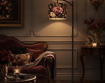 May include: A floor lamp with a thin black metal stand and a curved top arm. The cylindrical lampshade features a dark background with a vibrant floral pattern of pink, white, and yellow roses and green leaves, emitting a warm, soft glow.