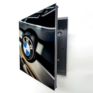 May include: A framed wall art print featuring a close-up of a BMW engine component. The image showcases the BMW logo in a blue and white circle, set against a backdrop of black and silver engine parts. The frame is black.
