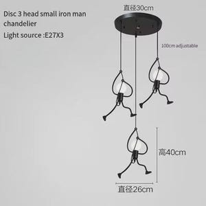 K&ouml;nnte beinhalten: Schwarze Eisenmann-H&auml;ngeleuchte mit drei Lichtern. Die Leuchte hat eine Deckenplatte mit 30 cm Durchmesser und verstellbare Kabel. Jede Leuchte hat eine stilisierte Figur mit einer Gl&uuml;hbirne. Die Gesamth&ouml;he betr&auml;gt 40 cm.