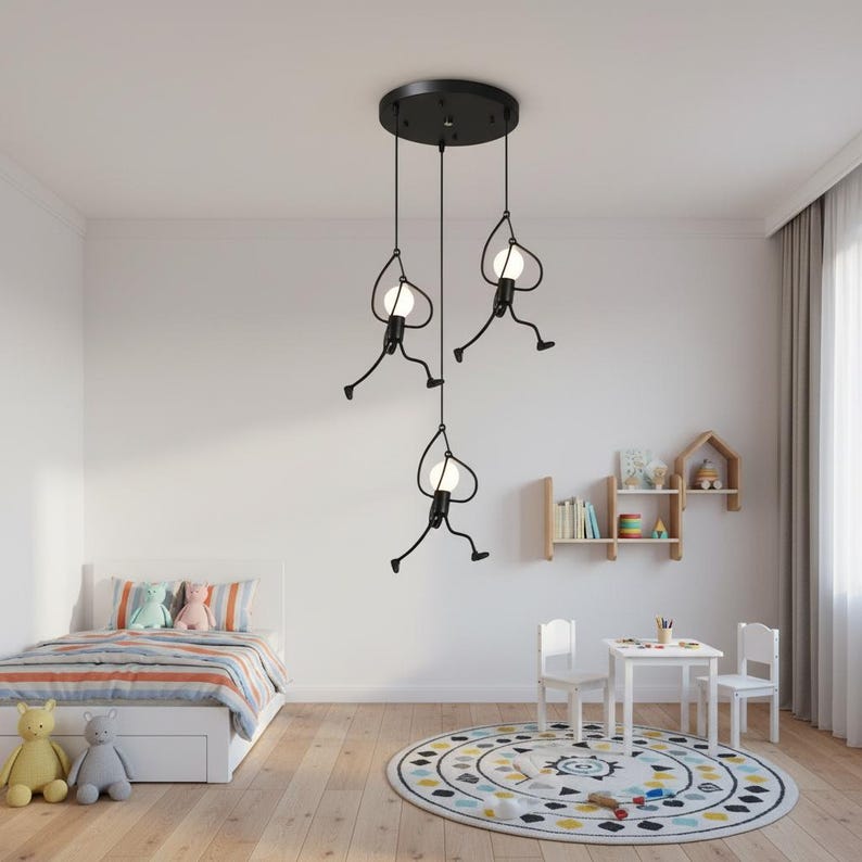 K&ouml;nnte beinhalten: Eine schwarze Pendelleuchte mit drei Lichtern und einem skurrilen Design. Jedes Licht hat eine stilisierte Figur mit einer runden Gl&uuml;hbirne, die von einer kreisf&ouml;rmigen Deckenhalterung abgeh&auml;ngt ist. Die Lampe befindet sich in einem Kinderzimmer.