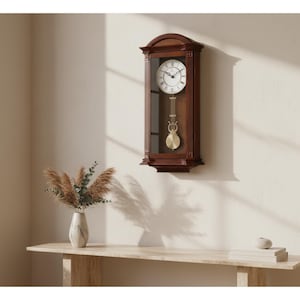 May include: A rectangular wall clock with a dark brown wooden frame and an arched top. The clock face is white with black Roman numerals and hands. A glass panel reveals a gold-colored pendulum hanging inside the central section of the clock.