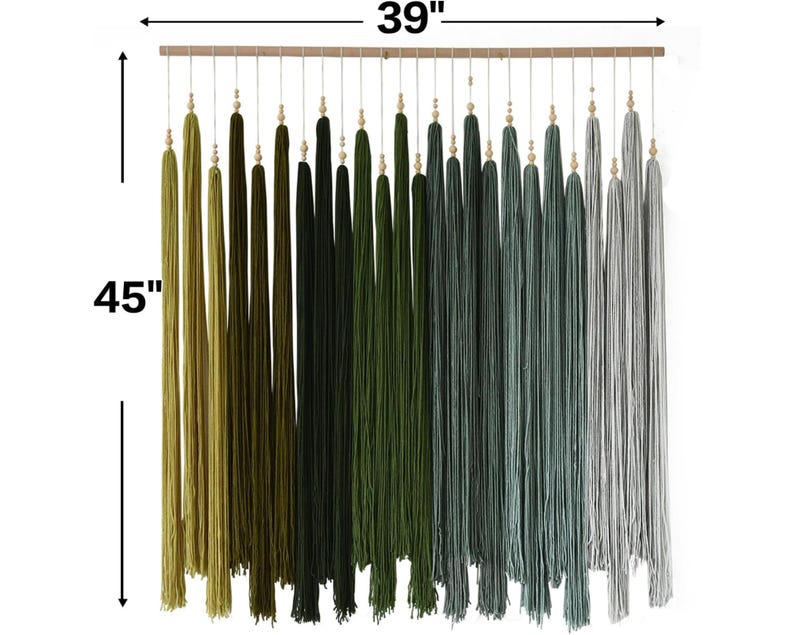 Puede incluir: Un tapiz de pared con una barra de madera horizontal y numerosos hilos verticales en un degradado de color que va del verde oliva al negro, verde oscuro, verde azulado y gris claro. Cada hilo tiene una peque&ntilde;a cuenta de madera. Mide 99 cm de ancho por 114 cm de alto.