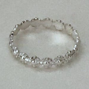 May include: A silver ring with a delicate, textured design. The ring is made of small, rounded shapes that create a continuous pattern.