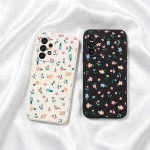May include: Two rectangular smartphone cases featuring a repeating floral pattern. One case is cream-colored with pink, orange, and blue flowers, while the other is black with the same floral design. Both cases have a multi-lens camera cutout.