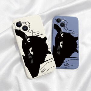 May include: Two rectangular smartphone cases featuring a graphic illustration of a black cat with white eyes and whiskers. One case is cream-coloured, and the other is periwinkle blue. Both cases have a camera cutout in the upper left corner.