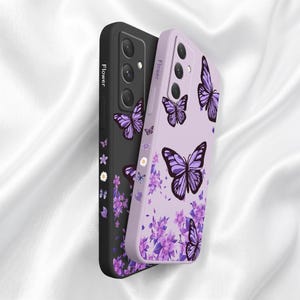 以下が含まれることがあります： 黒とラベンダー色の2つの携帯電話ケースが表示されています。ラベンダー色のケースは蝶と花の模様です。黒いケースは蝶と花の模様です。「Flower」の文字が各ケースの側面に縦に印刷されています。