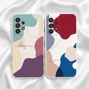 Op de afbeelding: Twee smartphonehoesjes met abstracte organische vormen in gedempte tinten blauw, rood, crème en paars. Het linkerhoesje toont de tekst "love you" in cursief, terwijl het rechterhoesje de tekst "Have a nice day with you!" in een eenvoudig lettertype bevat.