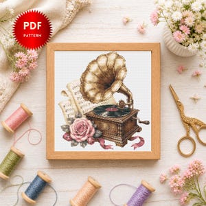 May include: A cross-stitch pattern featuring a vintage gramophone with a large golden horn, a black vinyl record, sheet music, and a pink rose. The design is framed in a square wooden frame, with a red circular badge labeled PDF PATTERN.