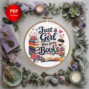 May include: A circular wooden embroidery hoop containing a cross-stitch pattern with the text Just a Girl Who Loves Books. The design features a stack of colorful books, an open book, a coffee cup, flowers, stars, and black reading glasses.