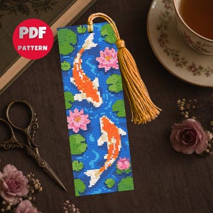 May include: A rectangular bookmark featuring a cross-stitch pattern of two orange and white koi fish swimming among pink water lilies and green lily pads on a blue water background, finished with a golden yellow tassel at the top.