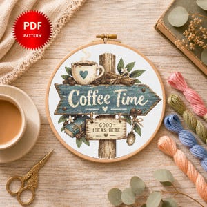 May include: A cross-stitch pattern in a wooden embroidery hoop featuring a blue wooden sign with the text Coffee Time and a smaller sign below reading Good Ideas Here. The design includes a coffee mug, coffee beans, cinnamon sticks, and leaves.