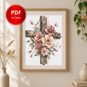 Può includere: Un modello PDF digitale raffigurante una croce in legno invecchiato e testurizzato, decorata con un grappolo di fiori rosa tenue e color pesca con foglie verdi. L'opera d'arte è esposta all'interno di una cornice in legno chiaro.