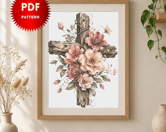 May include: A digital PDF pattern featuring a cross made of weathered, textured wood adorned with a cluster of soft pink and peach-colored flowers and green leaves. The artwork is displayed within a light-colored wooden frame on a wall.