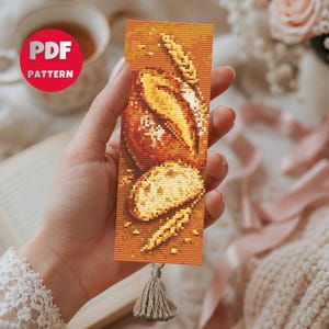 Puede incluir: Un marcapáginas rectangular de punto de cruz con un diseño detallado de una hogaza de pan, una rebanada de pan y espigas de trigo en tonos amarillo dorado, naranja y marrón. El marcapáginas incluye una pequeña borla beige en la parte inferior.