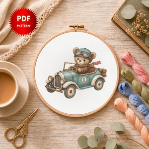 May include: A cross-stitch pattern in a wooden embroidery hoop featuring a brown teddy bear wearing a blue aviator cap and goggles, driving a vintage light blue race car with the number one on the side and a red polka dot scarf around its neck.