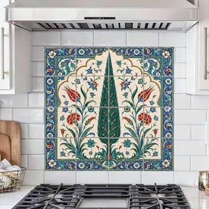 Könnte beinhalten: Ein quadratisches Wandfliesen-Wandbild mit einer zentralen grünen Zypresse, flankiert von roten Tulpen und blauen Blumenmotiven auf cremefarbenem Grund, umrahmt von einer dekorativen blau-weißen Bordüre, installiert als Fliesenspiegel über einem Herd.