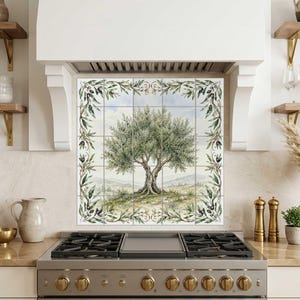Puede incluir: Un protector contra salpicaduras de cocina con una pintura de acuarela de un olivo. La obra de arte está enmarcada por ramas de olivo y aceitunas. El árbol se alza sobre un fondo de colinas y cielo azul.