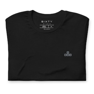 May include: A black t-shirt featuring a small, embroidered graphic of four computer keyboard keys arranged in a cross pattern with the letters W, A, S, and D. The inner neck label displays the text SIXTY STUDIO, Made in Nicaragua, and size XS.