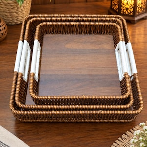 Puede incluir: Un juego de dos bandejas rectangulares encajables con laterales de ratán trenzado marrón oscuro y una base de madera oscura lisa y plana. Cada bandeja incluye dos asas integradas envueltas en material blanco en los lados.