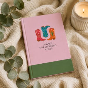 Puede incluir: Un cuaderno rosa con un borde inferior verde oscuro que presenta tres botas vaqueras ilustradas en rojo, azul cerceta y naranja con detalles de estrellas y cactus. El texto OLIVIA'S LINE DANCING NOTES está impreso en negro en el centro.