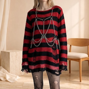 May include: Red and black striped sweater with distressed details. The long-sleeved sweater features a silver chain harness with a pentagram pendant. The sweater has a round neckline and a relaxed fit.