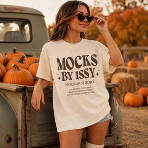 Op de afbeelding: Een crèmekleurig t-shirt met korte mouwen en donkerbruine tekst met de tekst MOCKS BY ISSY MOCKUP STUDIO USE EDITING PROGRAMS LIKE PHOTOSHOP, AFFINITY, CANVA TO ADD YOUR DESIGNS en kleine sterpictogrammen op de voorkant van het kledingstuk.