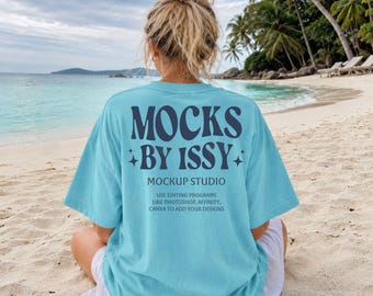 Mockup da camiseta Comfort Colors 1717 Azul Lagoa, vista traseira da camiseta na praia, mockup de camiseta para férias na costa.