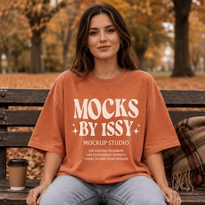 May include: An oversized burnt orange t-shirt featuring the white text MOCKS BY ISSY MOCKUP STUDIO USE EDITING PROGRAMS LIKE PHOTOSHOP, AFFINITY, CANVA TO ADD YOUR DESIGNS with small star icons, worn with blue denim jeans and a brown coffee cup.