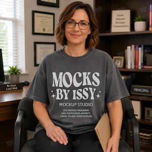 Op de afbeelding: Een antracietgrijs t-shirt met korte mouwen en witte tekst die luidt MOCKS BY ISSY MOCKUP STUDIO USE EDITING PROGRAMS LIKE PHOTOSHOP, AFFINITY, CANVA TO ADD YOUR DESIGNS, geaccentueerd met kleine vierpuntige stergraphics aan de zijkanten.