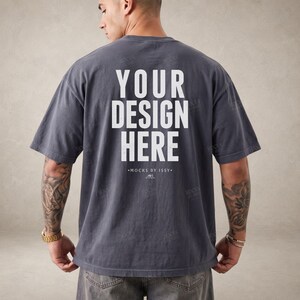 May include: A charcoal grey short-sleeve t-shirt featuring the white text "YOUR DESIGN HERE" printed on the back. Below the text, the smaller white text reads "MOCKS BY ISSY" with a small graphic icon. The shirt has a loose, relaxed fit.