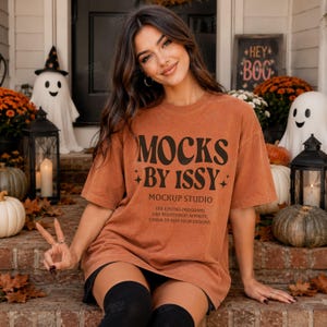 May include: A rust-colored short-sleeve t-shirt featuring black text that reads MOCKS BY ISSY MOCKUP STUDIO USE EDITING PROGRAMS LIKE PHOTOSHOP, AFFINITY, CANVA TO ADD YOUR DESIGNS with small star icons on the sides of the text.