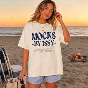May include: Cream-colored t-shirt with the text "MOCKS BY ISSY" in navy blue, along with the text "USE EDITING PROGRAMS LIKE PHOTOSHOP, AFFINITY, CANVA TO ADD YOUR DESIGN." The shirt is worn on a beach at sunset.