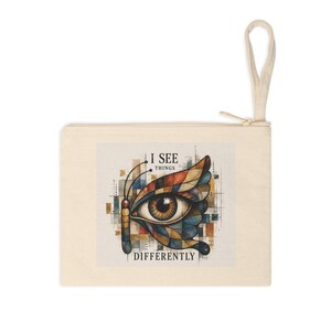 Può includere: Un astuccio con cerniera color crema con un colorato disegno a occhio di farfalla e la scritta "I SEE THINGS DIFFERENTLY". L'occhio di farfalla ha ali marroni, blu, arancioni e gialle. L'astuccio ha un passante color crema.