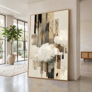 May include: Abstract art print in a gold frame. The artwork features vertical rectangular shapes in shades of beige, brown, and gray, with a large cloud-like form. A small silhouette of a person is visible. The art is displayed in a modern interior.