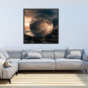 May include: A square framed wall art piece featuring a large, transparent glass sphere resting on dark rocks. The sphere reflects a sunset over a turbulent ocean with golden light, dark clouds, and crashing waves, all set within a thin black frame.
