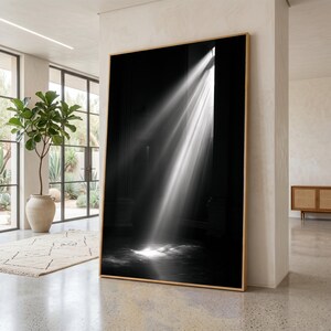 Puede incluir: Una gran pieza de arte mural rectangular que presenta una fotografía en blanco y negro de alto contraste de un haz de luz brillante que ilumina un espacio interior oscuro y sombreado, enmarcada en un marco de madera clara.