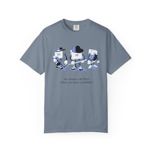 May include: Blue t-shirt featuring a humorous graphic of Ctrl, Alt, and Del keys as cartoon characters. The keys are depicted with hats and tools, with the text "You always call them when you have a problem!"
