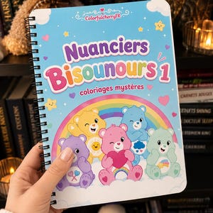 Peut inclure: Un carnet à spirales avec une couverture bleu clair portant le texte "Nuanciers Bisounours 1 coloriages mystères" et une illustration colorée de cinq personnages Bisounours, incluant des ours jaunes, bleus, roses, violets et verts.