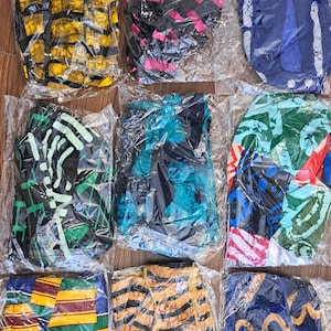 May include: A collection of various fabric head wraps in clear plastic packaging. The head wraps feature diverse patterns and colors, including black and white, yellow and black, pink and black, blue and white, green and black, and blue and yellow.